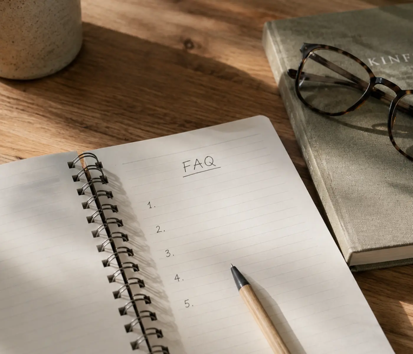 Open notebook labelled “FAQ” beside a pen and reading glasses, representing frequently asked legal questions.